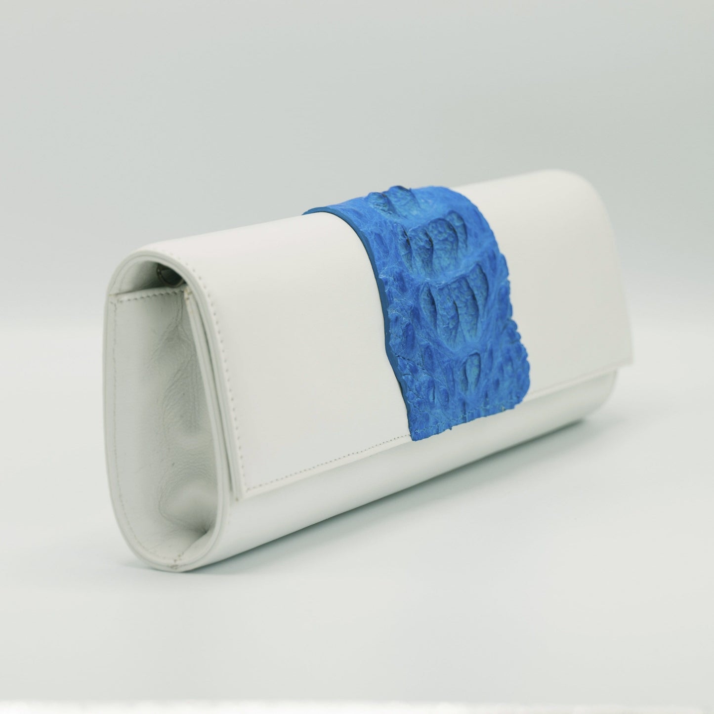 Blue and white Kate Crocodile and leather clutch.Handcrafted from Italian saffino leather. Sustainably sourced crocodile ascent, magnetic closure, interior pocket, and removable shoulder strap with a 22” drop. 